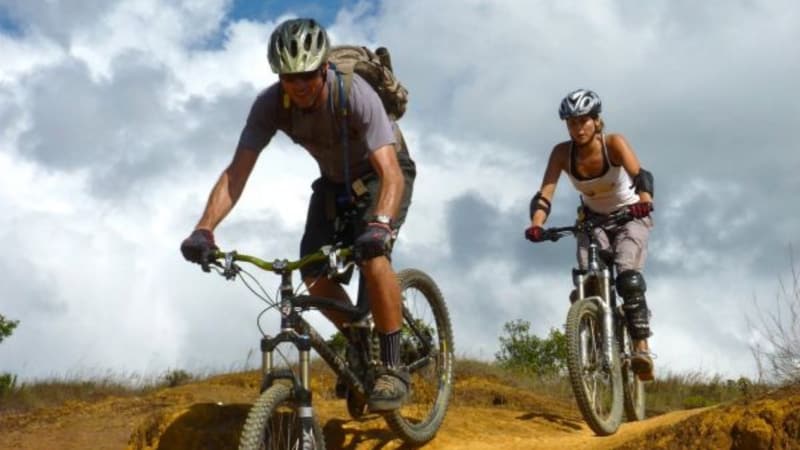 Two mountain bikers riding a dirt trail under a cloudy sky.