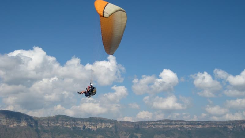 A tandem paraglider high above a wide canyon rim.