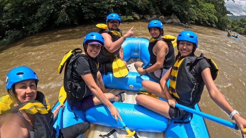 A raft crew in blue helmets paddling a whitewater river.