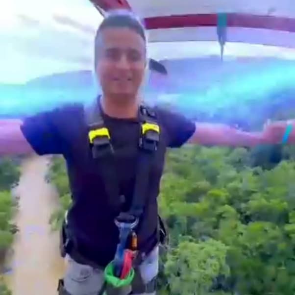 A Macondo team member in a harness on a bungee platform, a brown river and green valley far below.