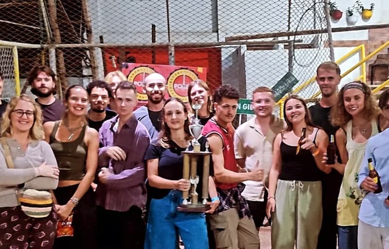 A big group of travellers at a tejo club, one in the middle holding up a tall trophy.